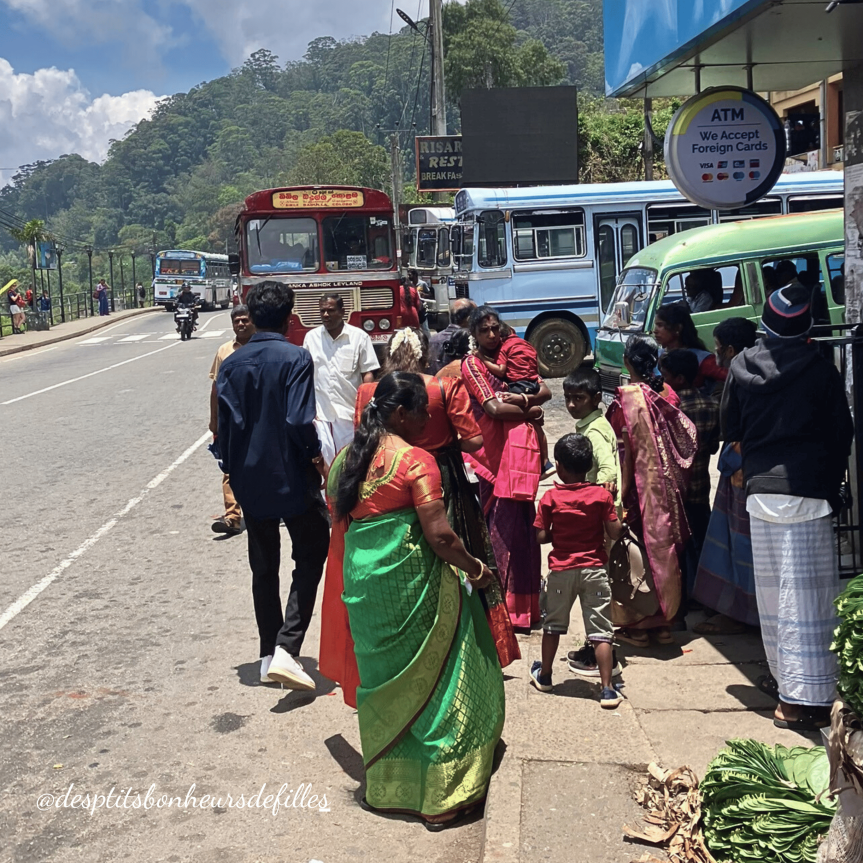 Groupe de personnes en vêtements traditionnels sri-lankais, rassemblées près d'une route, avec des bus en arrière-plan 