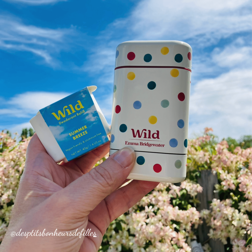 Un déodorant rechargeable Wild avec son étui coloré et une recharge Summer Breeze, devant un arrière-plan de fleurs et d'un ciel bleu.